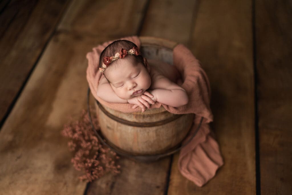 bébé nouveau-né dans un petit seau en bois – séance photo naissance artistique en studio