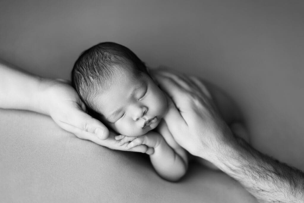 photo naissance noir et blanc bébé dans les mains de son papa – photographe nouveau-né en studio 77