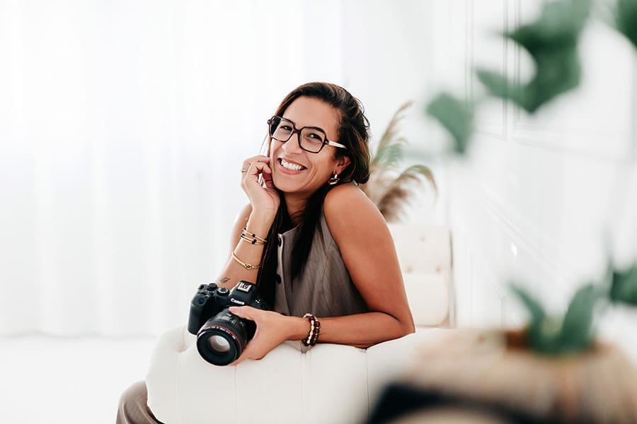 magali tinti assise sur un canapé avec son appareil photo et souriante